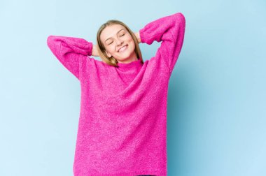 Genç sarışın kadın mavi arka planda izole edilmiş. Kendinden emin, elleri başının arkasında..