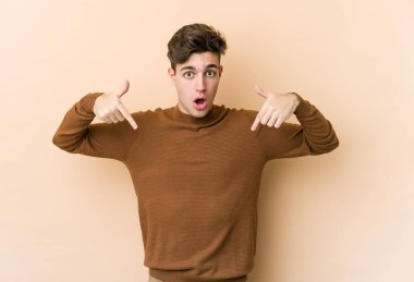 Beyazlı genç bir adam bej arka planda izole edilmiş. Parmakları aşağıda, olumlu hisler içinde..