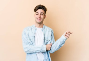 Beyazların arka planında izole edilmiş genç beyaz adam işaret parmağıyla işaret ederek gülümsüyor..