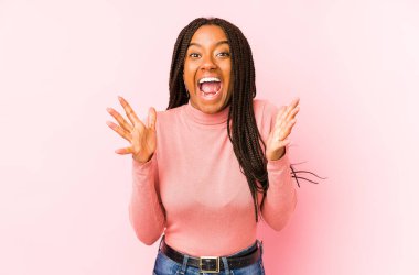 Genç Afrikalı Amerikalı kadın pembe bir arka planda izole edilmiş zaferi veya başarıyı kutluyor, şaşırmış ve şok olmuş..