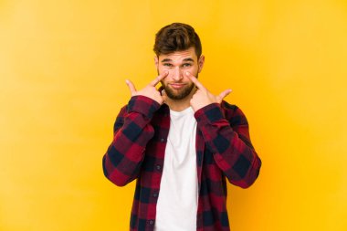 Kafkasyalı genç adam sarı arka planda izole edilmiş, ağlıyor, bir şeyden memnun değil, acı ve kafa karışıklığı kavramı..