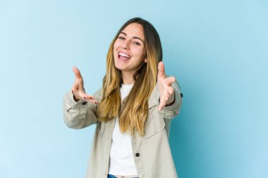 Mavi arka planda izole edilmiş genç beyaz kadın kameraya sarıldığı için kendinden emin..