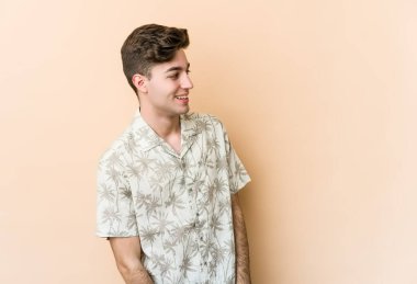 Beyaz tenli, bej arka planda izole bir genç. Gülümsüyor, neşeli ve keyifli görünüyor..