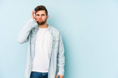 Genç beyaz adam mavi arka planda izole edilmiş ve parmakları dudaklarında bir sır saklıyor..