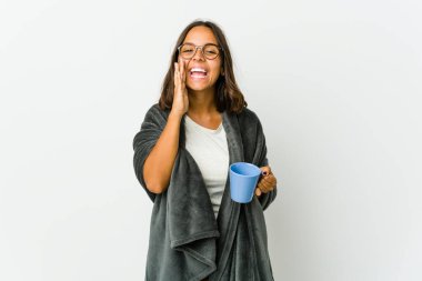 Beyaz arka planda battaniyeli genç Latin bir kadın heyecanlı bir şekilde bağırıyor..