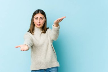 Genç beyaz kadın kollarıyla ölçek yapıyor, mutlu ve kendinden emin..