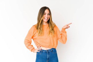 Beyaz arka planda izole edilmiş genç beyaz kadın işaret parmağıyla işaret ederek gülümsüyor..