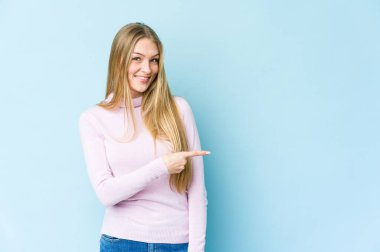 Mavi arka planda izole edilmiş genç sarışın kadın gülümsüyor ve boş alanda bir şeyler gösteriyor..
