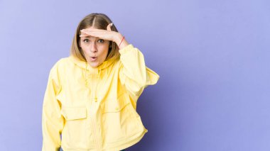 Mor arka planda soyutlanmış genç sarışın kadın uzaklara bakıyor ve elini alnına koyuyor..