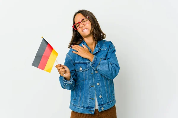 若いラテン語の女性が肩の痛みを持つ白い背景に隔離されたドイツ語のフラグを保持 — ストック写真