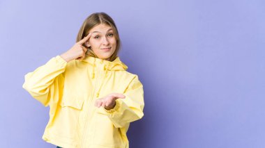 Mor arka planda izole edilmiş genç sarışın kadın elinde bir ürün tutuyor..