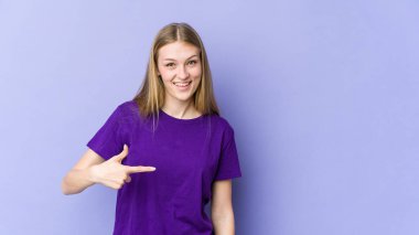 Mor arka planda izole edilmiş genç sarışın kadın gömlek fotokopisini elle gösteriyor, gururlu ve kendinden emin.