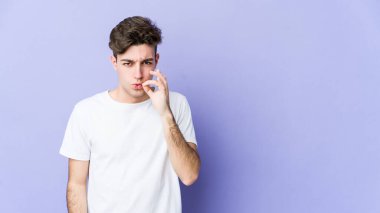 Mor arka planda izole edilmiş genç, beyaz bir adam dudaklarında parmaklarıyla bir sır saklıyor..