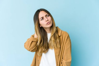 Genç beyaz kadın mavi arka planda izole edilmiş. Stres yüzünden boynu ağrıyor. Masaj yapıyor ve elle dokunuyor..