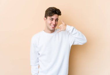 Beyazlı genç bir adam bej arka planda izole edilmiş. Cep telefonu hareketini parmaklarıyla gösteriyor..