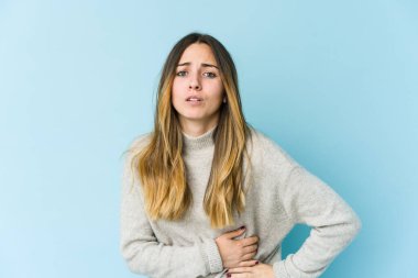 Mavi arka planda karaciğer ağrısı çeken, karnı ağrıyan beyaz bir kadın..