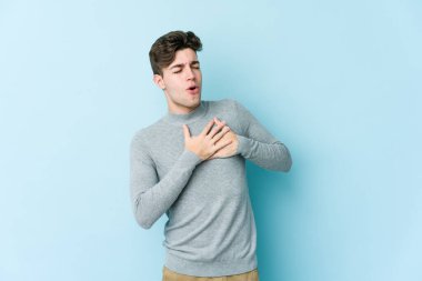 Mavi arka planda izole edilmiş beyaz bir genç, dost bir ifadeye sahip, avuçlarını göğsüne bastırıyor. Aşk konsepti.