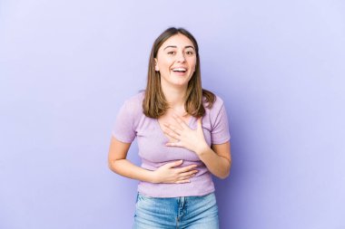 Genç beyaz kadın mutlu bir şekilde gülüyor ve ellerini karnının üstünde tutarak eğleniyor..