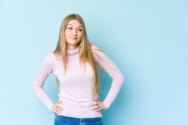 Mavi arka planda izole edilmiş genç sarışın kadın kafası karışmış, şüpheli ve güvensiz hissediyor..