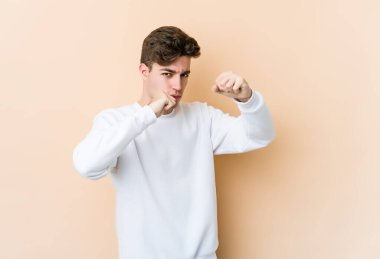 Beyazlı genç bir adam bej arka planda izole edilmiş. Yumruk atıyor, sinirleniyor, tartışıyor, boks yapıyor..