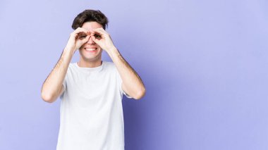 Mor arka planda izole edilmiş genç beyaz adam gözlerinde sorun olmadığını gösteriyor.