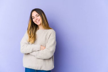 Mor arka planda izole edilmiş genç beyaz bir kadın. Kendine güveniyor, kararlılıkla kollarını kavuşturuyor..