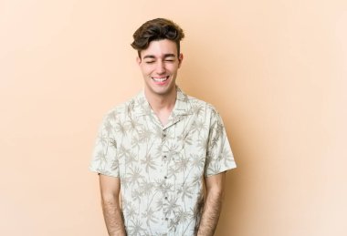 Beyazların arka planında izole edilmiş genç beyaz adam gülüyor ve gözlerini kapatıyor, rahatlamış ve mutlu hissediyor..