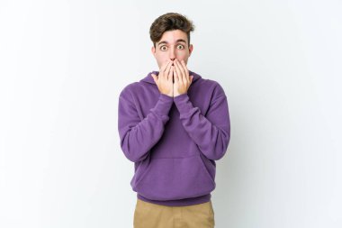 Beyaz arka planda izole edilmiş genç beyaz adam elleriyle ağzını kapatırken şok oldu..