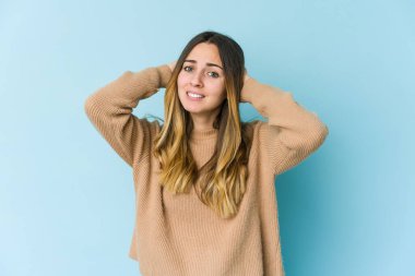 Kafkasyalı genç bir kadın mavi arka planda izole edilmiş kafasının arkasına dokunuyor, düşünüyor ve bir seçim yapıyor..