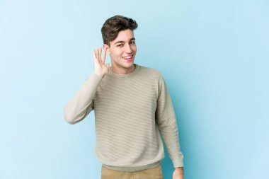 Mavi arka planda izole edilmiş genç beyaz adam bir dedikoduyu dinlemeye çalışıyor..