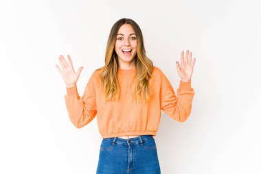Beyaz arka planda izole genç beyaz kadın hoş bir sürpriz alıyor, heyecanlı ve el kaldırıyor..