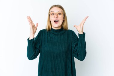 Genç sarışın kadın, beyaz bir arkaplanda zaferi ya da başarıyı kutlarken şaşırdı ve şok oldu..