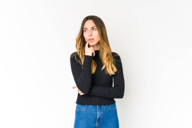 Beyaz arka planda soyutlanmış beyaz tenli genç bir kadın şüpheli ve şüpheci bir ifadeyle yana bakıyor..