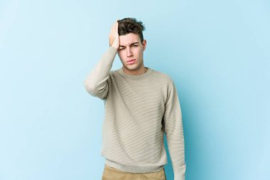 Kafkasyalı genç adam mavi arka planda izole edilmiş. Yorgun ve uykulu. Elini başının üstünde tutuyor..