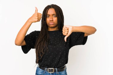 Beyaz arka planda izole edilmiş genç Afrikalı Amerikalı kadın baş parmağını kaldırıyor ve baş parmağını aşağı gösteriyor, zor seçim konsepti
