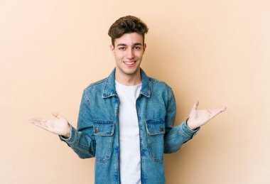 Beyazlı genç bir adam bej arka planda izole edilmiş, kollarıyla ölçek yapıyor, mutlu ve kendinden emin hissediyor..