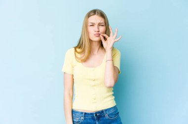 Mavi arka planda izole edilmiş genç sarışın kadın parmakları dudaklarında bir sır saklıyor..