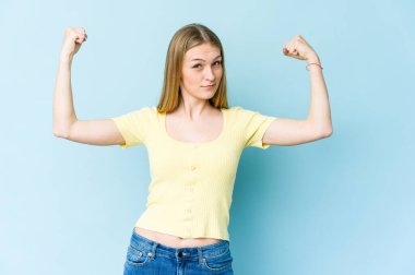 Mavi arka planda izole edilmiş genç sarışın kadın güçlü hareketlerini kollarıyla gösteriyor, kadınsı gücün sembolü.