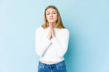 Mavi arka planda izole edilmiş genç sarışın kadın el ele tutuşup ağzının kenarında dua ediyor, kendinden emin hissediyor..