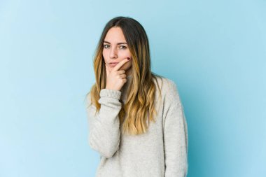 Kafkasyalı genç bir kadın, mavi arka planda izole edilmiş. Bir strateji planlıyor, bir işin nasıl olacağını düşünüyor..