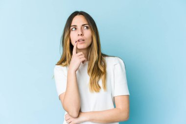 Mavi arka planda soyutlanmış beyaz bir kadın şüpheli ve şüpheci bir ifadeyle yana bakıyor..