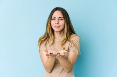 Kafkasyalı genç bir kadın mavi arka planda izole edilmiş. Elinde avuç içi olan bir şeyle kameraya sunuyor..