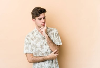 Beyazlı genç adam bej arka planda izole edilmiş şüpheli ve şüpheci bir ifadeyle yana bakıyor..