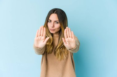 Mavi arka planda izole edilmiş genç beyaz kadın elini uzatmış, dur işareti göstererek seni engelliyor..