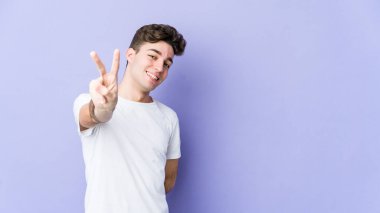 Mor arka planda izole edilmiş genç beyaz adam neşeli ve kaygısız parmakları olan bir barış sembolü gösteriyor..