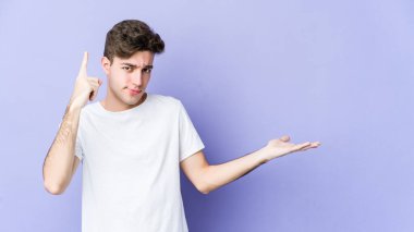 Mor arka planda izole edilmiş genç beyaz adam elinde bir ürün tutuyor..