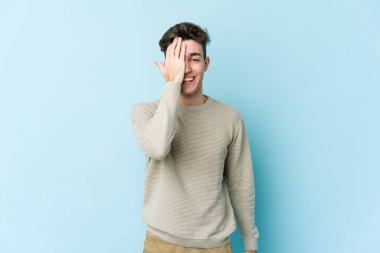 Mavi arka planda izole edilmiş genç beyaz adam yüzünün yarısını palmiye ile kaplayarak eğleniyor..