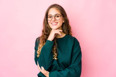 Genç beyaz kadın mutlu ve kendinden emin gülümsüyor, elleriyle çenesine dokunuyor..