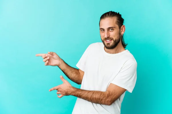 Young man with long hair look excited pointing with forefingers away.