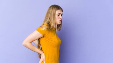 Mor arka planda izole edilmiş, sırt ağrısı çeken genç sarışın kadın..